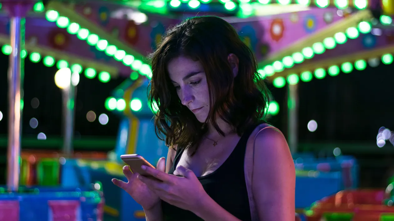 Stock photo of a young woman looking her smartphone with fairy lights in the background. Lifestyle, technology