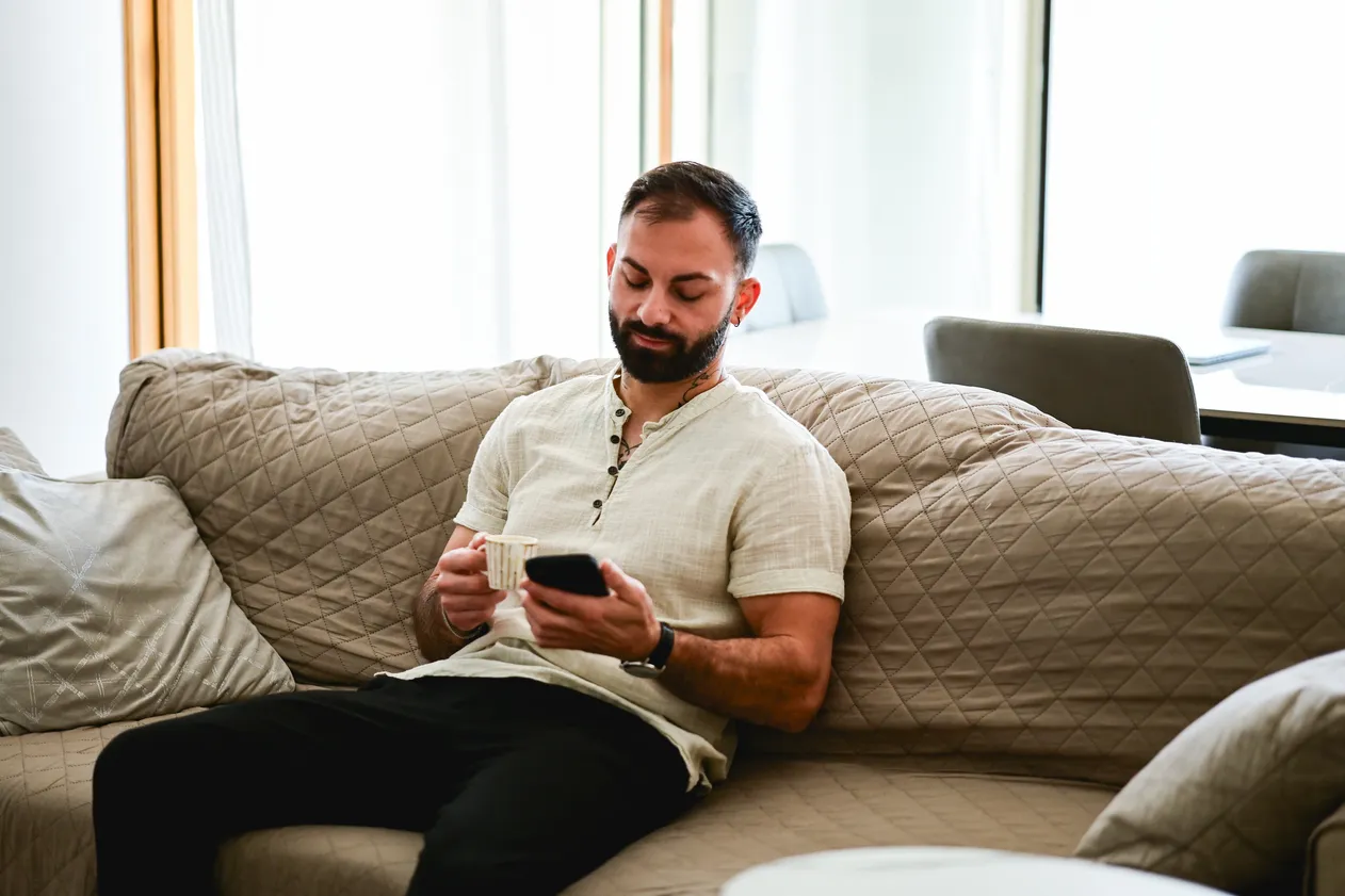 Man relaxing at home, enjoying a coffee and browsing his mobile phone