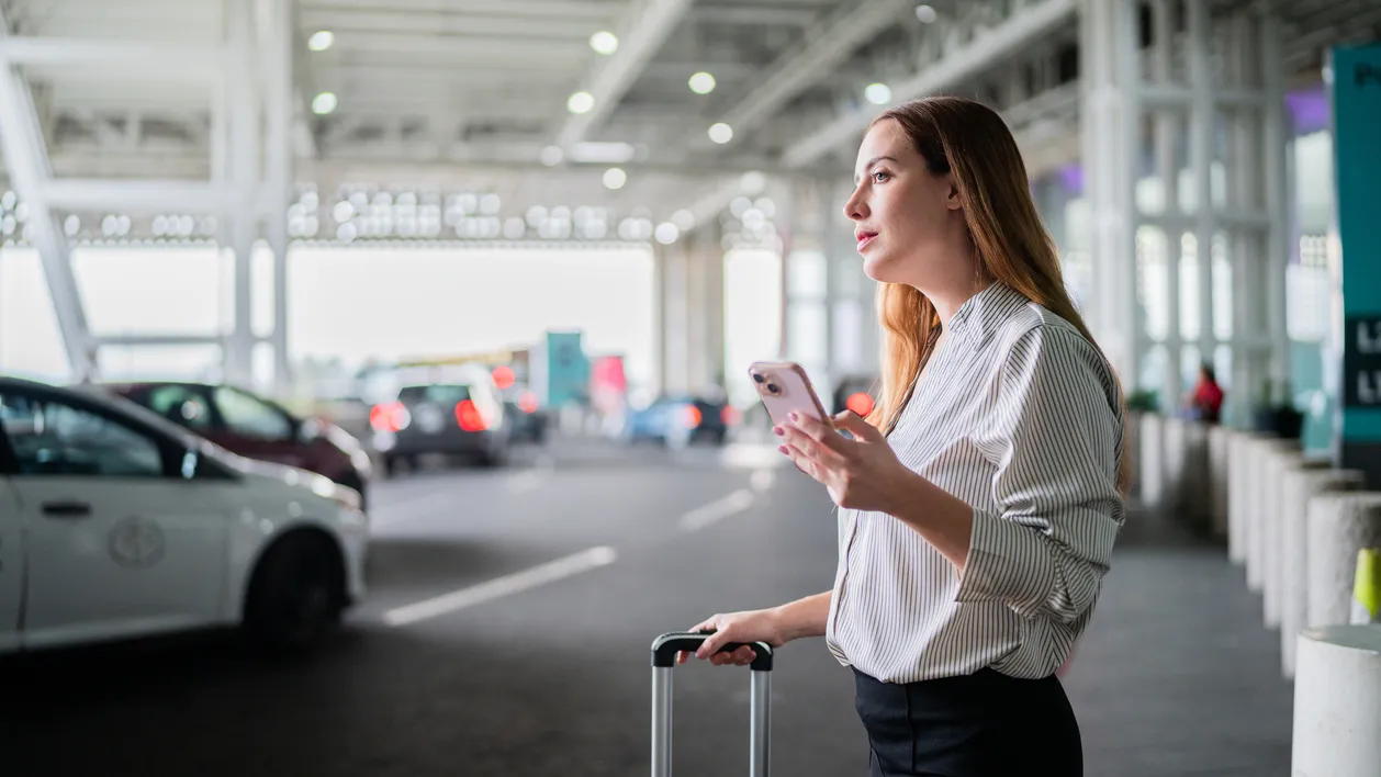 Mid adult businesswoman using mobile phone waiting taxi at airport