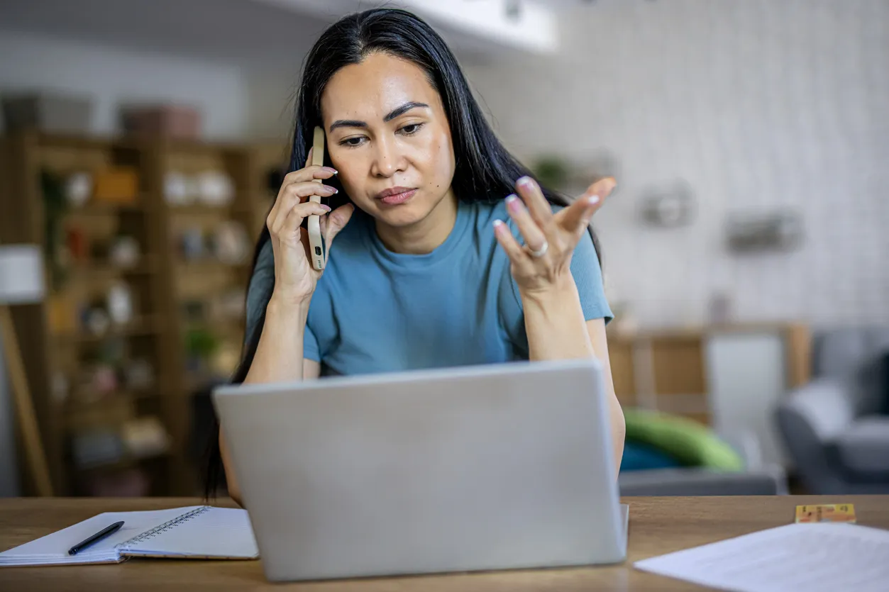 Remote employee looking worried while talking on a mobile phone during work from home, illustrating business challenges, problem solving, and professional communication.