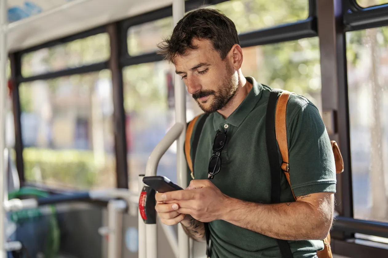A serious man in public transportation is typing on the phone.