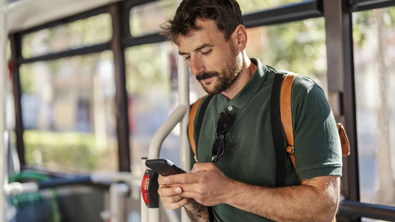 A serious man in public transportation is typing on the phone.