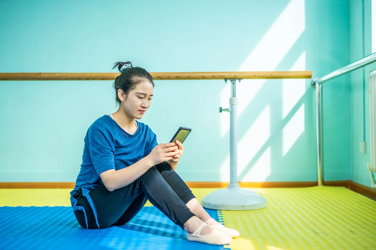Beautiful Asian dancer using smartphone in rehearsal hall