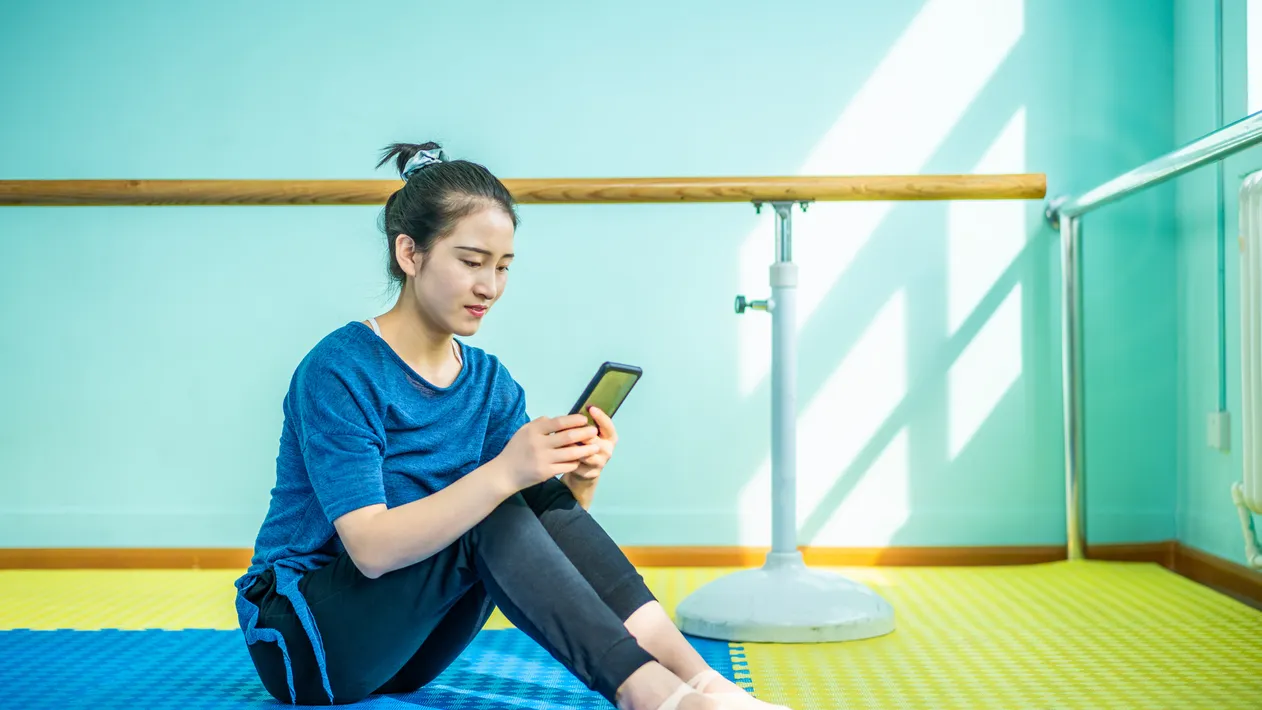 Beautiful Asian dancer using smartphone in rehearsal hall