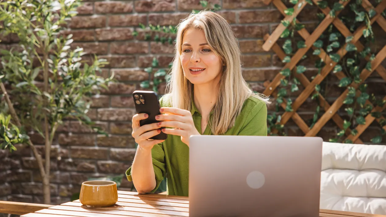 Confident middle-aged woman sitting comfortably at desk on the balcony at the backyard.