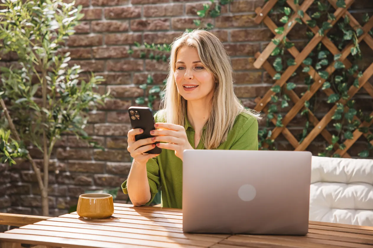 Confident middle-aged woman sitting comfortably at desk on the balcony at the backyard.